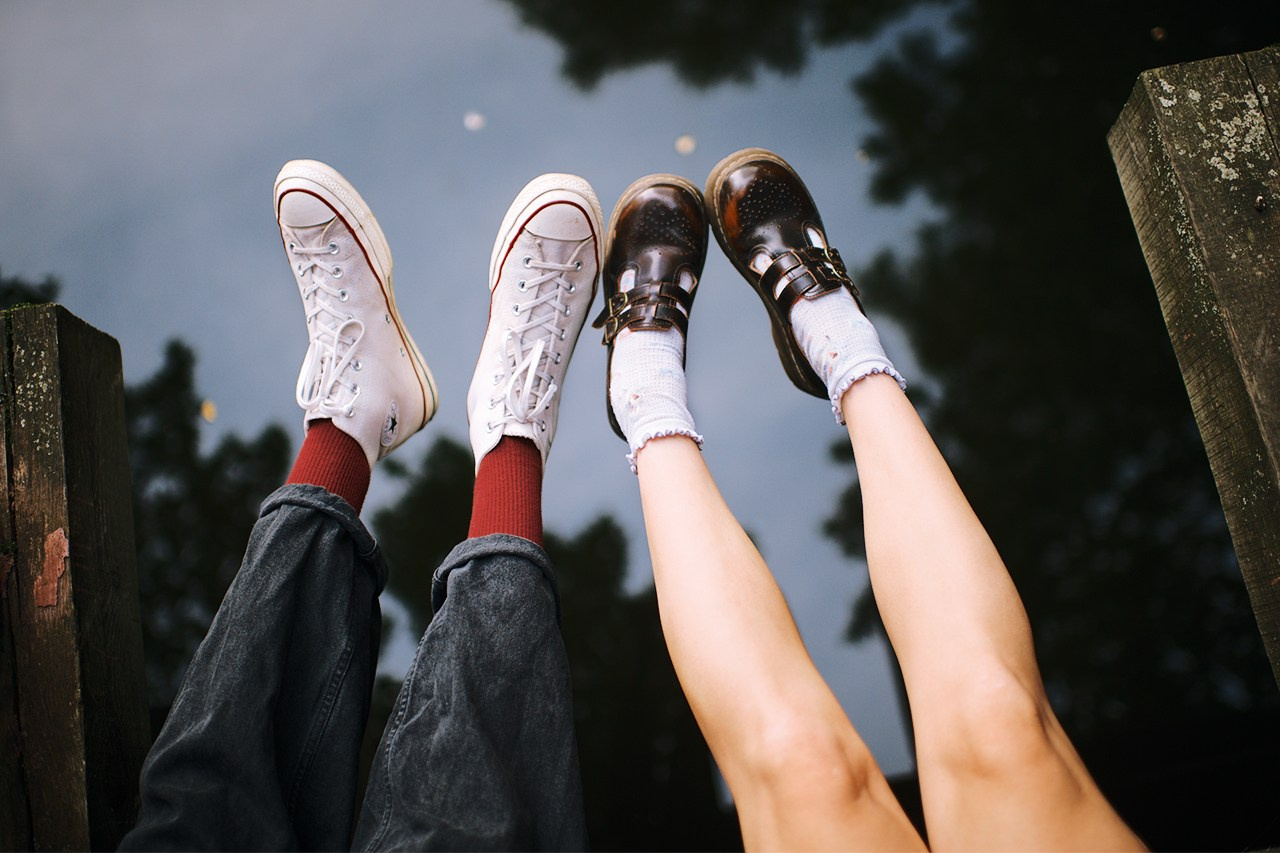 Ноги парня в белых кедах и девушки с коричневых туфлях на фоне пруда