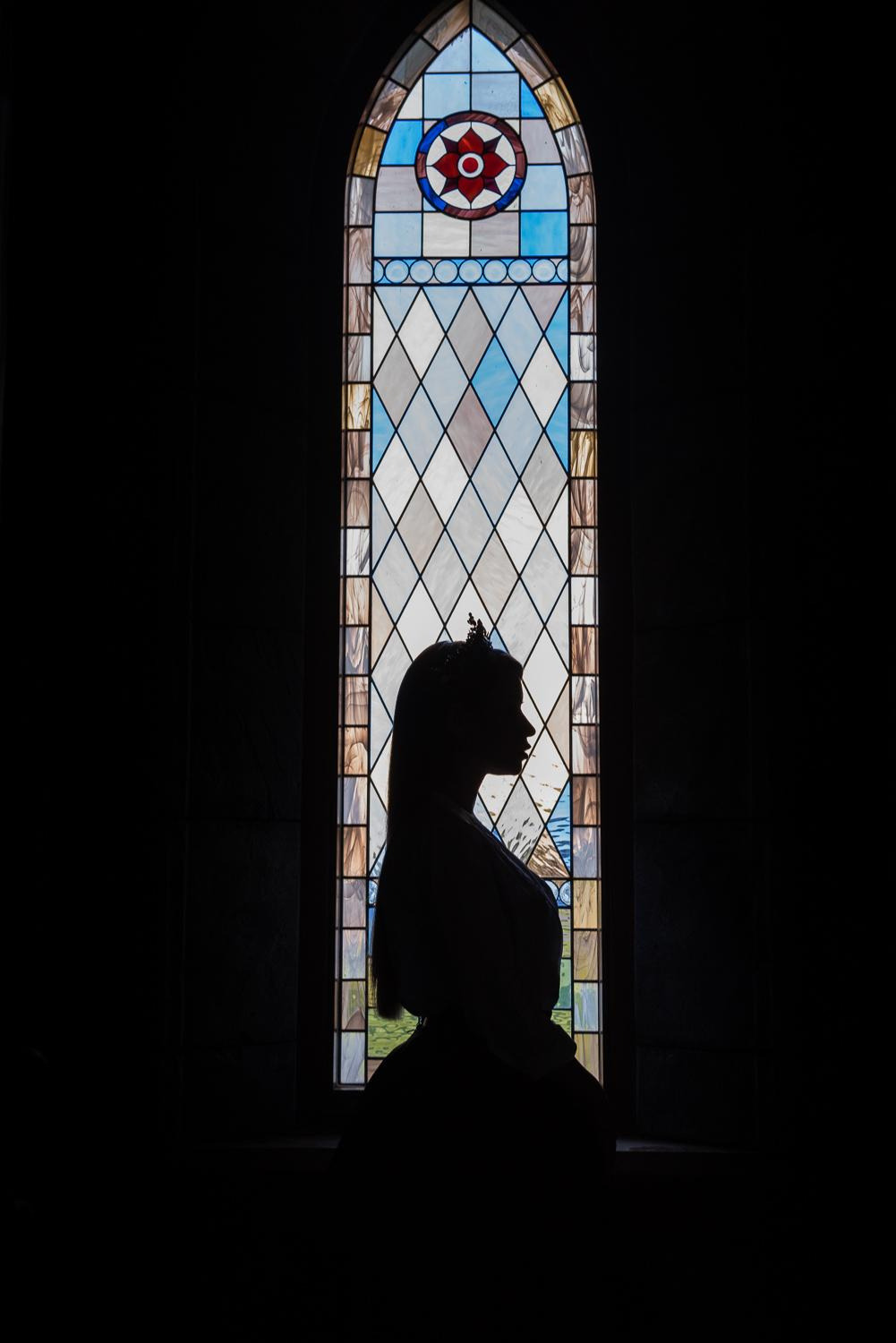 Силуэт девушки у витражного окна замка Гарибальди, подчеркивающий величие и красоту исторического интерьера.