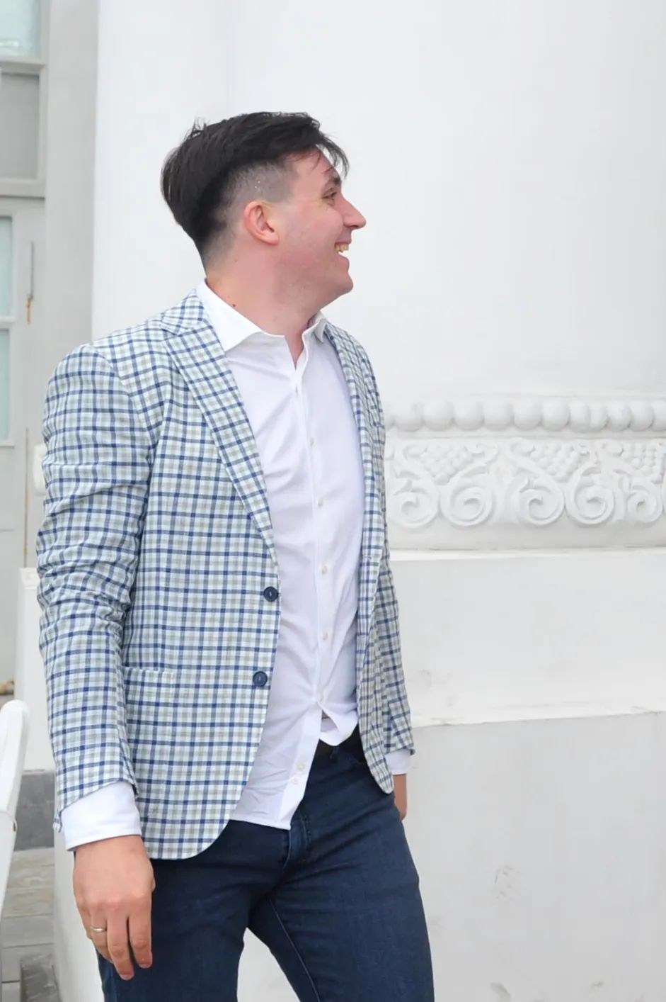 Свадьба на ВДНХ, жених в клетчатом пиджаке смеется, стоя у белой колонны