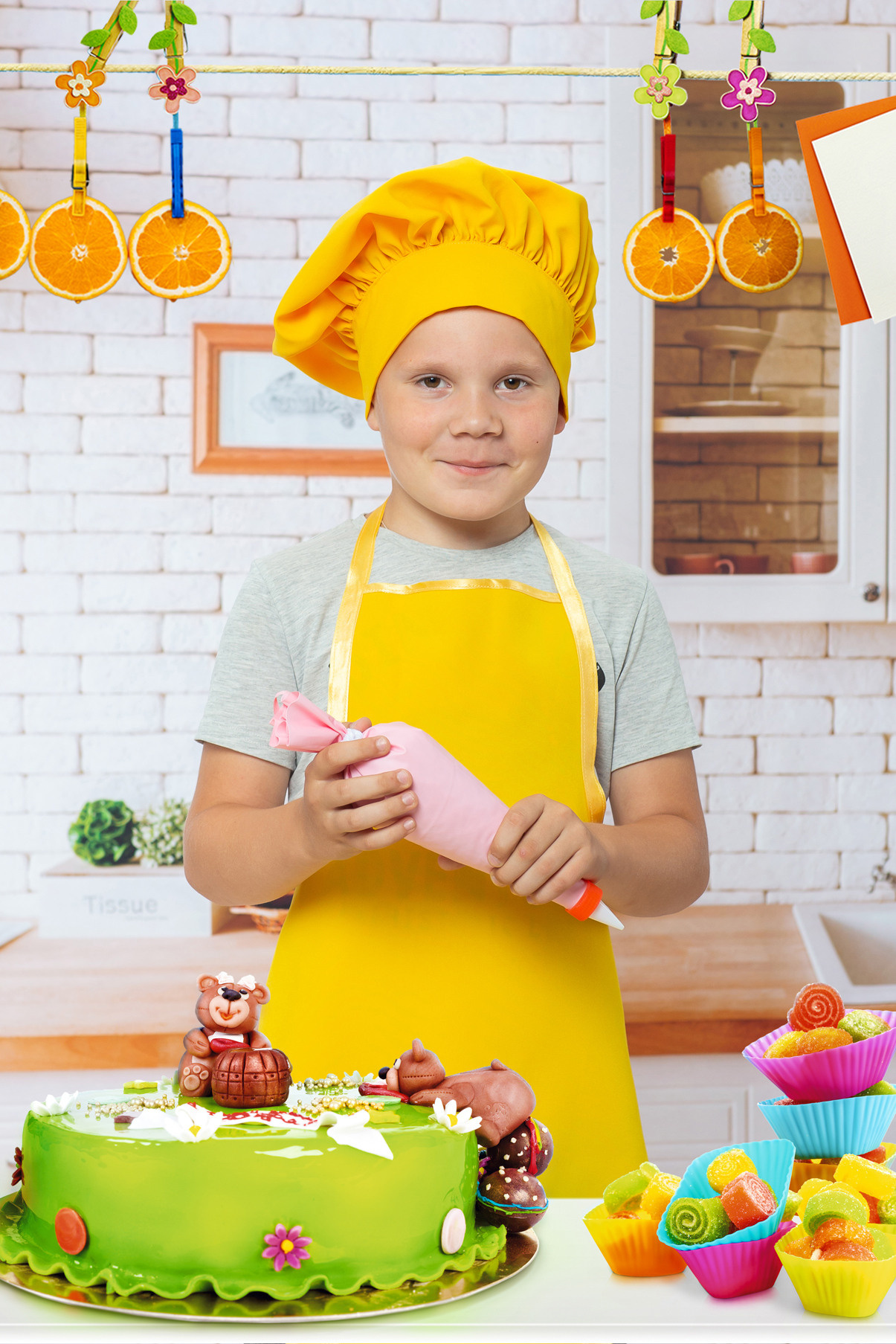 Детская тематическая костюмированная фотосессия на кухне. Поварята. Мальчик в желтом фартуке повара украшает кремом торт.