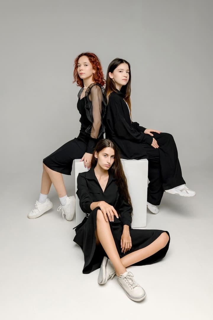 Юные девушки в черном, сидят на тумбе позирую в фотостудии.