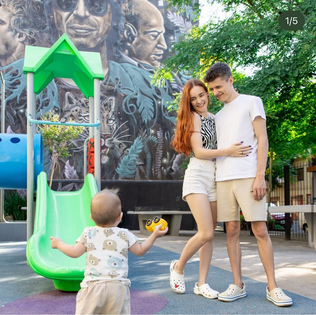 Малыш бежит к маме и папе которые обнимаются на детской площадке в Буэнос-Айресе