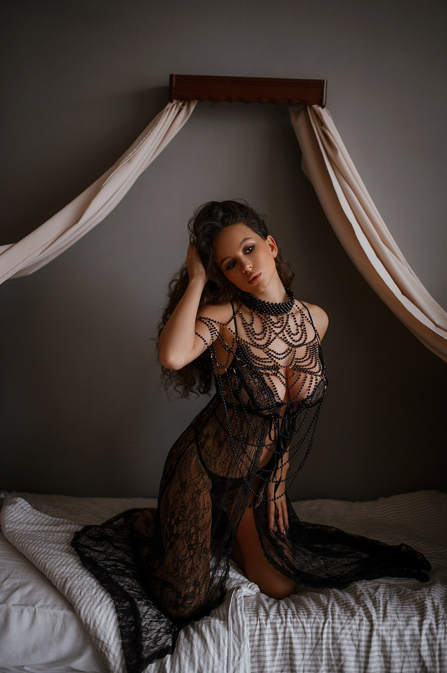 Модель в чёрном кружевном платье на кровати — чувственная поза и мягкие тени