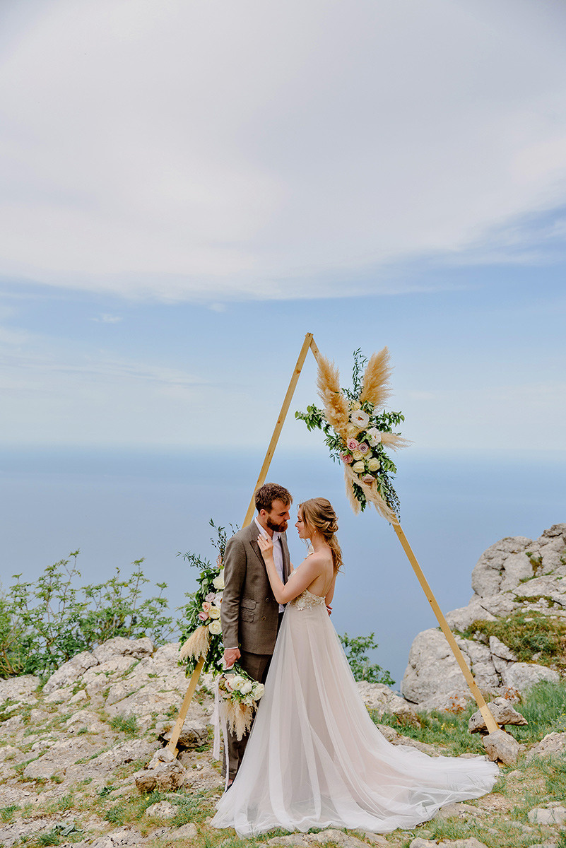 Молодожены стоят у арки на выездной регистрации брака в горах 