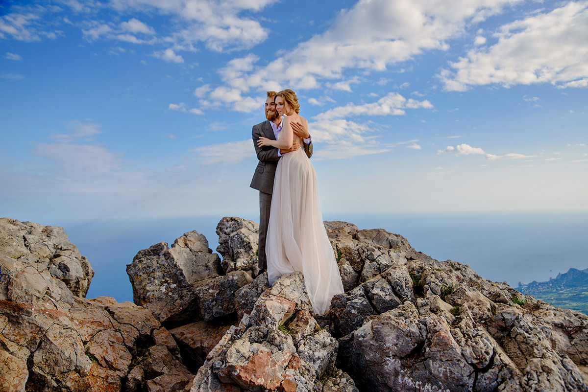 Влюбленная пара обнимается на фоне неба в горах.