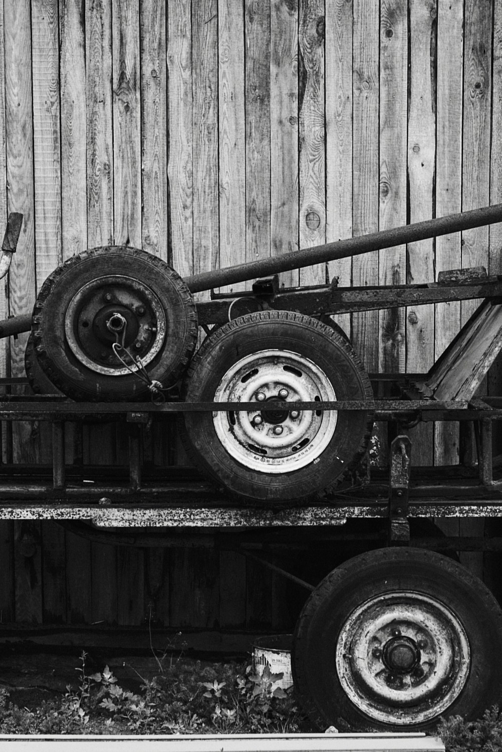 Колёса, закреплённые на металлической раме, на фоне вертикально уложенных деревянных досок; снимок в чёрно-белых тонах.