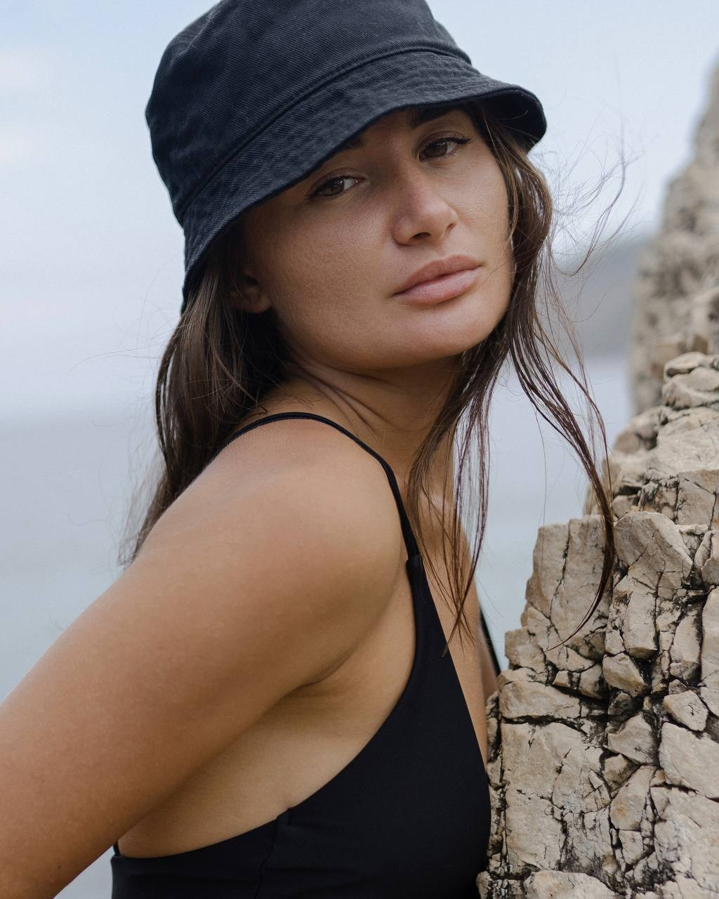 Портрет девушки в тёмной панаме у скал