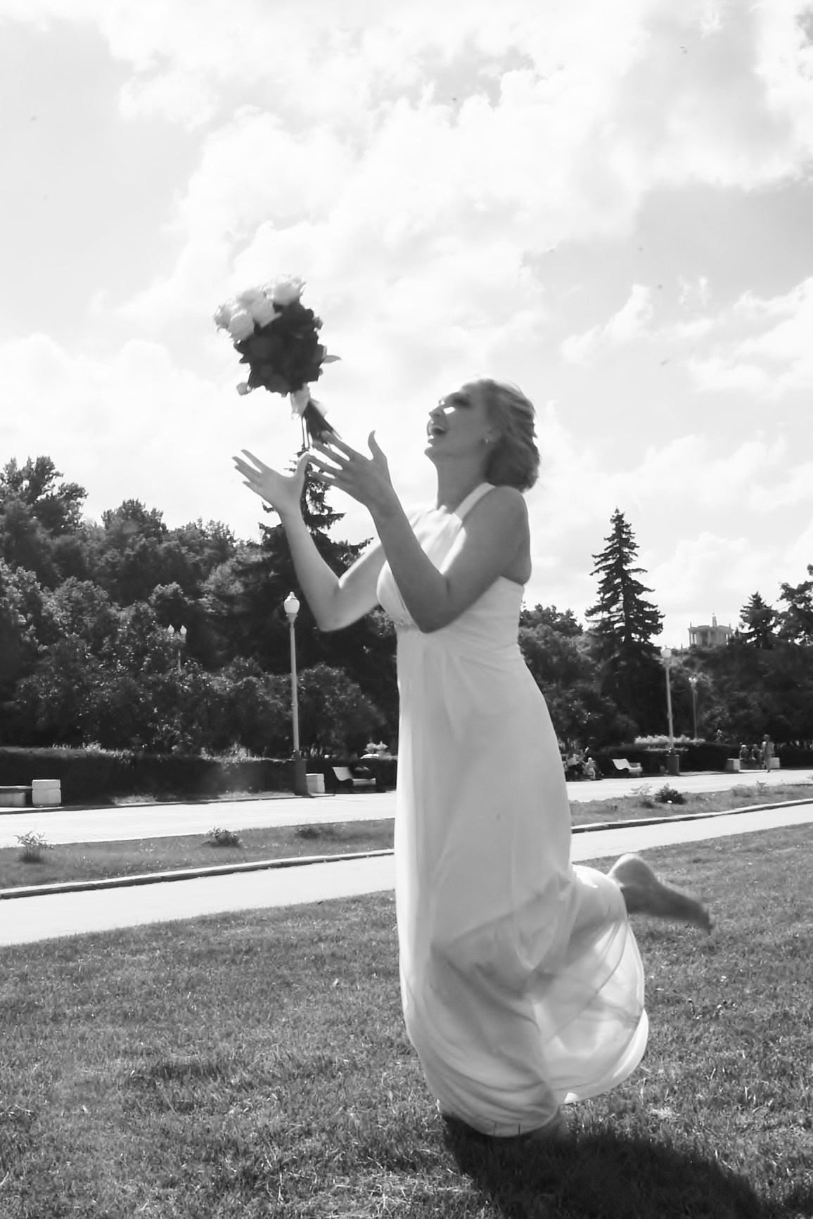 Свадьба на Воробьёвых Горах рядом с МГУ, невеста кидает свадебный букет на фоне деревьев и неба, черно-белая фотография