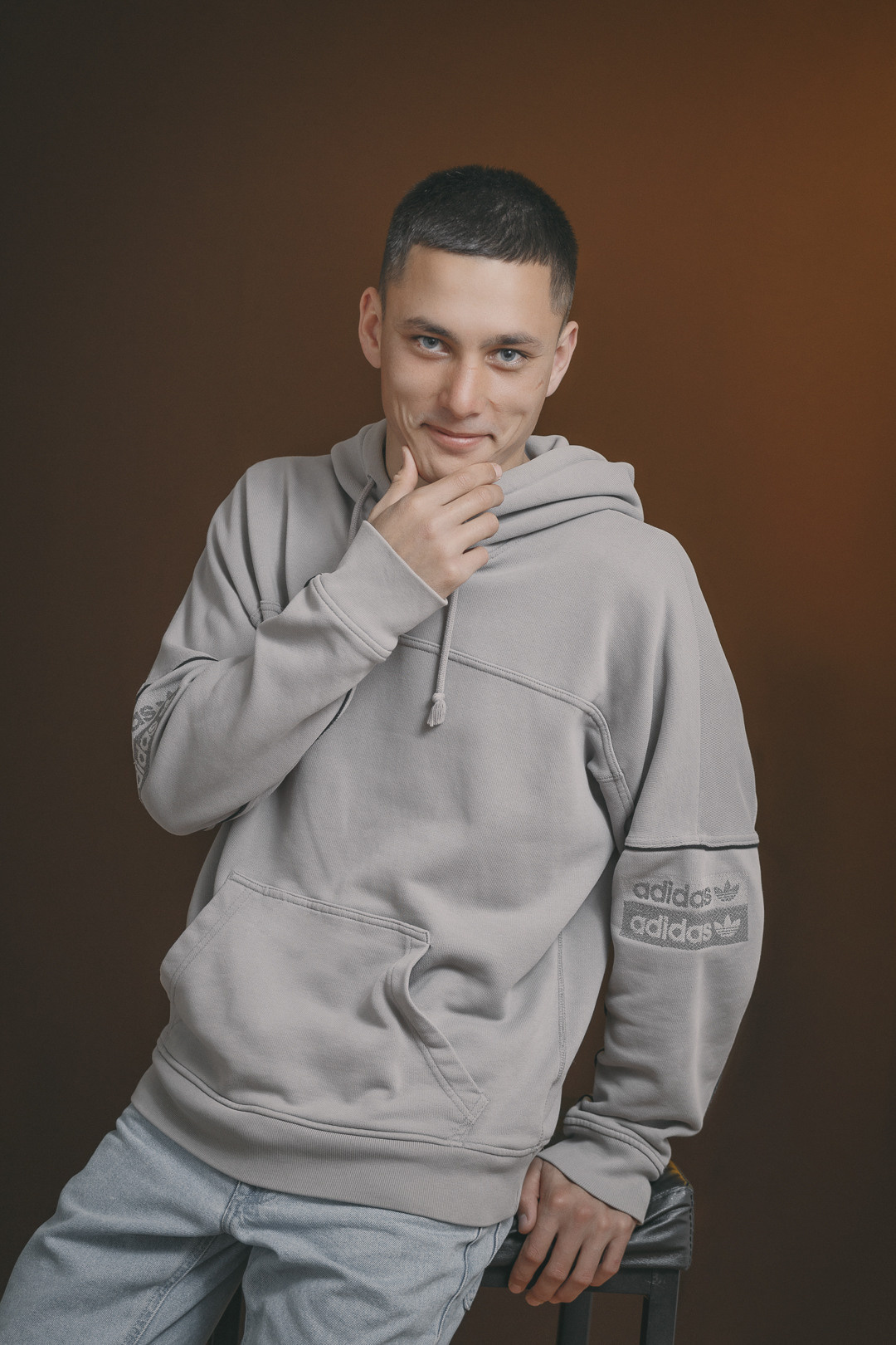 Молодой человек в джинсах и спортивной кофте позирует