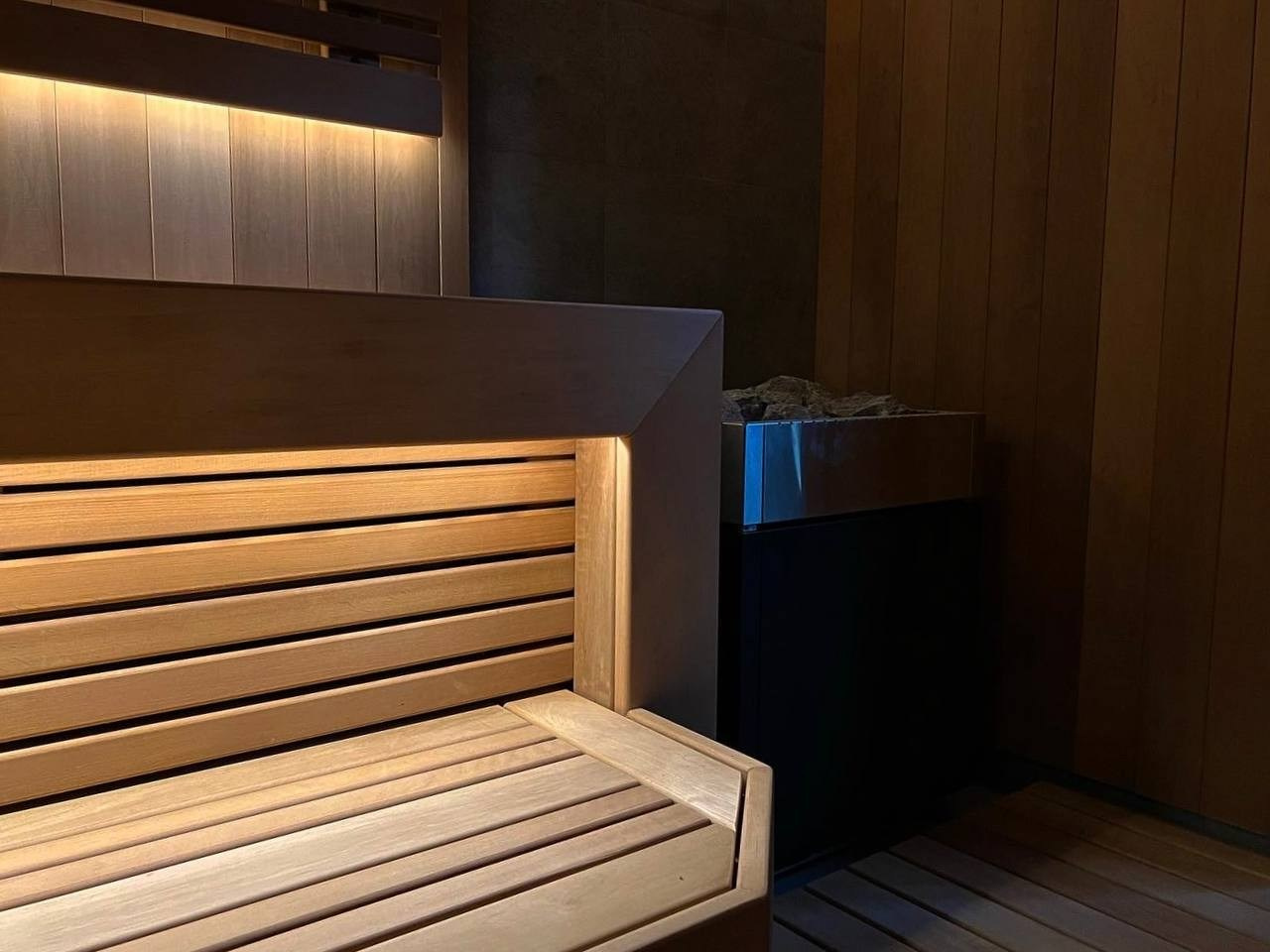 Сауна в Керро из разноширокой термоольхи. Ламповый свет термостойких лент и закарнизная подсветка плитки из талькохлорита 300×300мм. SaunaTopMasters