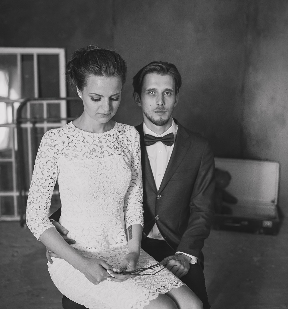 невеста в ажурном платье держит в руках ветки и сидит на коленях у жениха