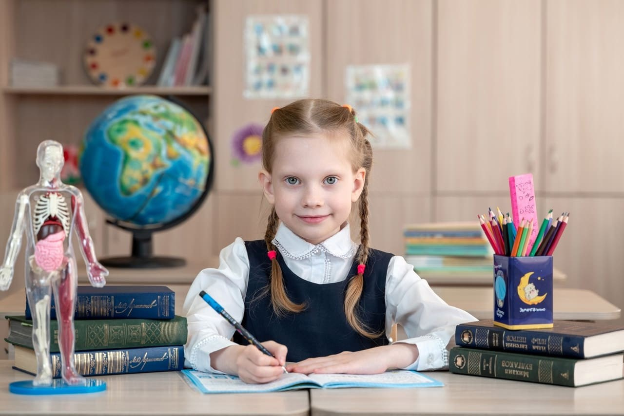 Школьница с глобусом мило улыбается держа ручку в правой руке.