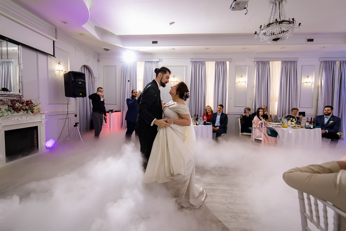 Жених и невеста танцуют первый танец в ресторане Санкт-Петербурга. Горизонтальный кадр. Жених и невеста смотрят друг на друга. Белый дым на полу.