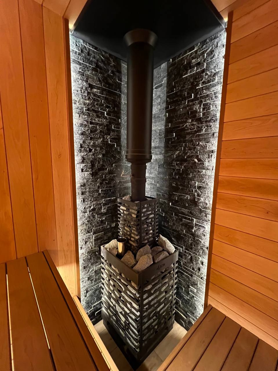 Семейная баня в Рощино из ольхи с можжевеловым панно, яркой печной зоной, закарнизной подсветкой и печью от производителя Aston. SaunaTopMasters