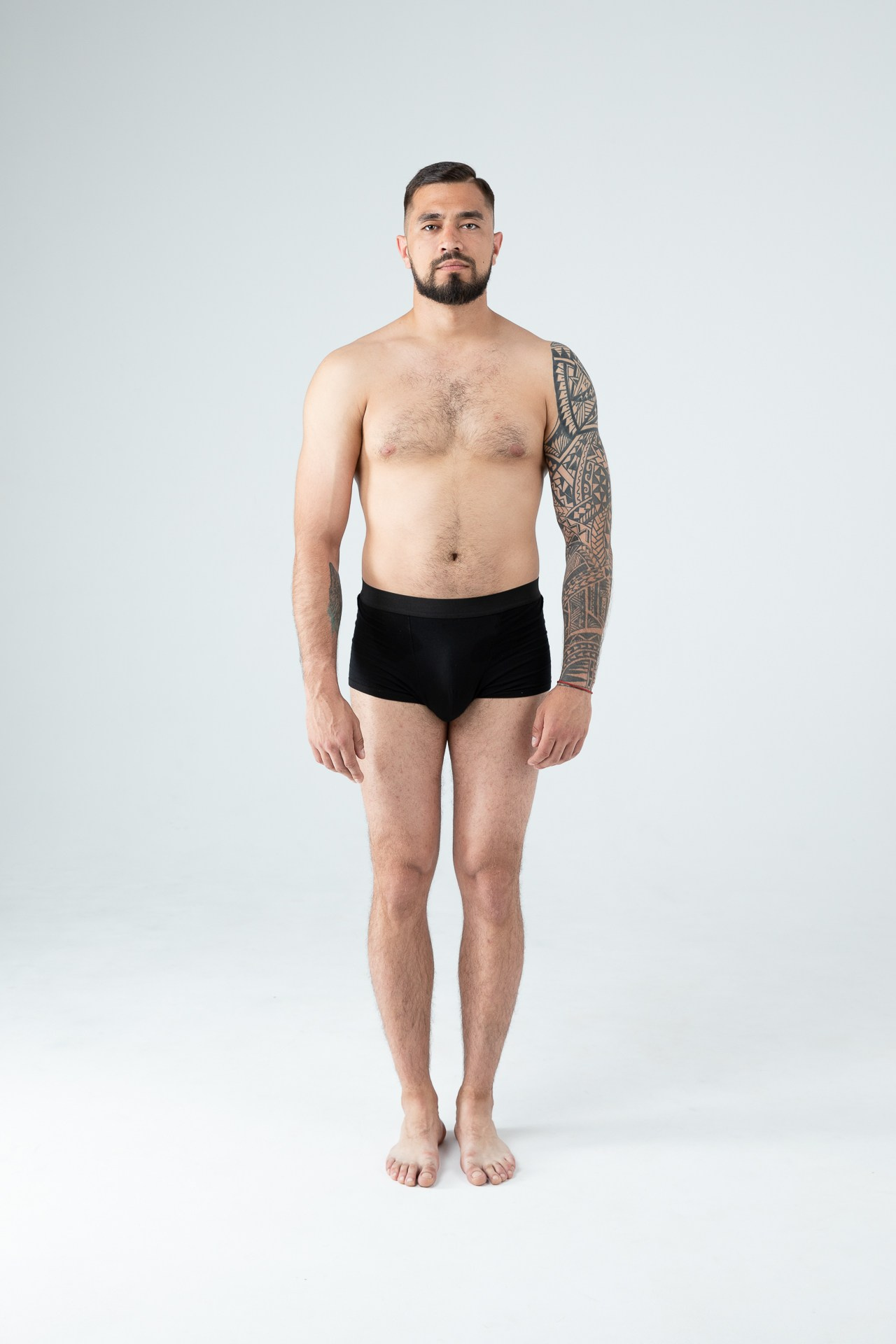 Мужчина модель с бородой с татуировками в черных трусах