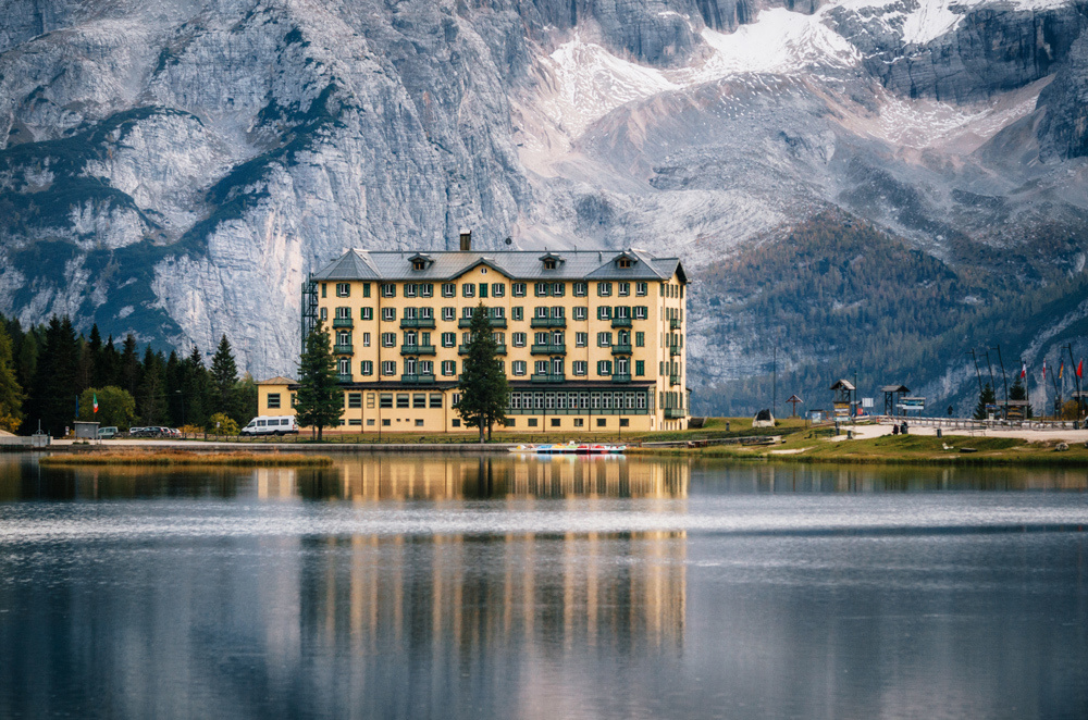 The View of Misurina lake with the large building of The Institute Pius XII through bushes at sunset. Dolomites, Italy.
