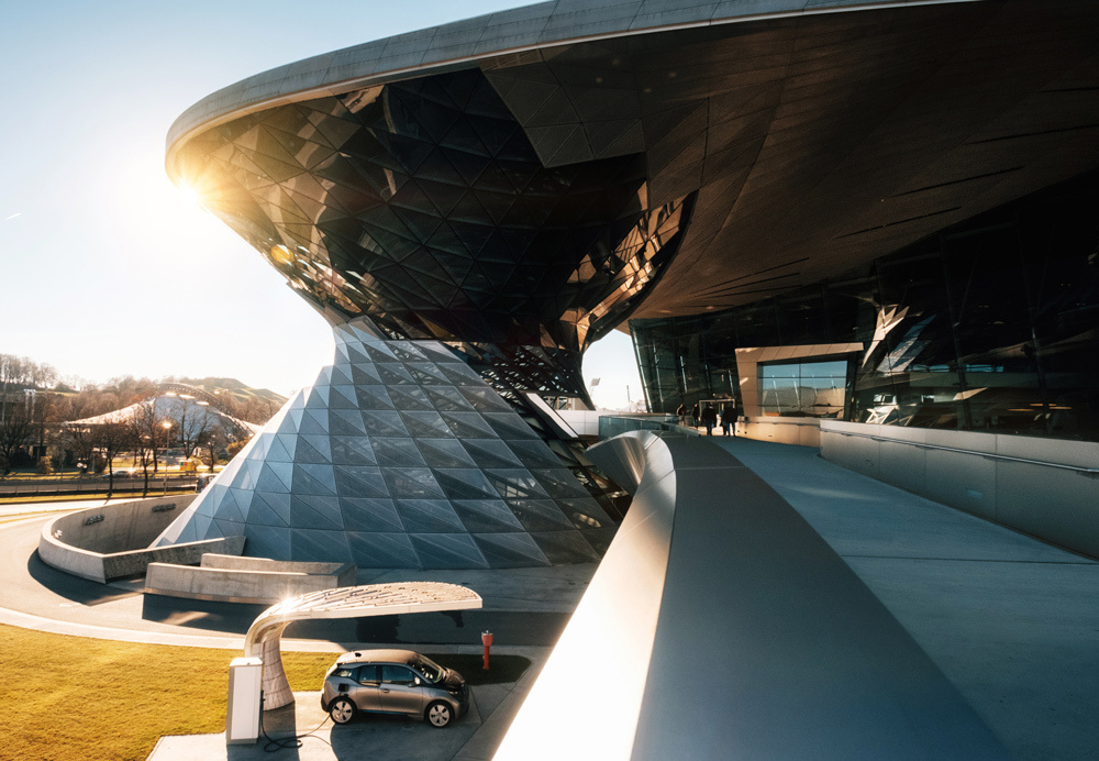 Munich, Germany. The BMW i3 electric car standing at a charging station at BMW Welt World of BWM with an exhibition and the museum buildings at sunset.