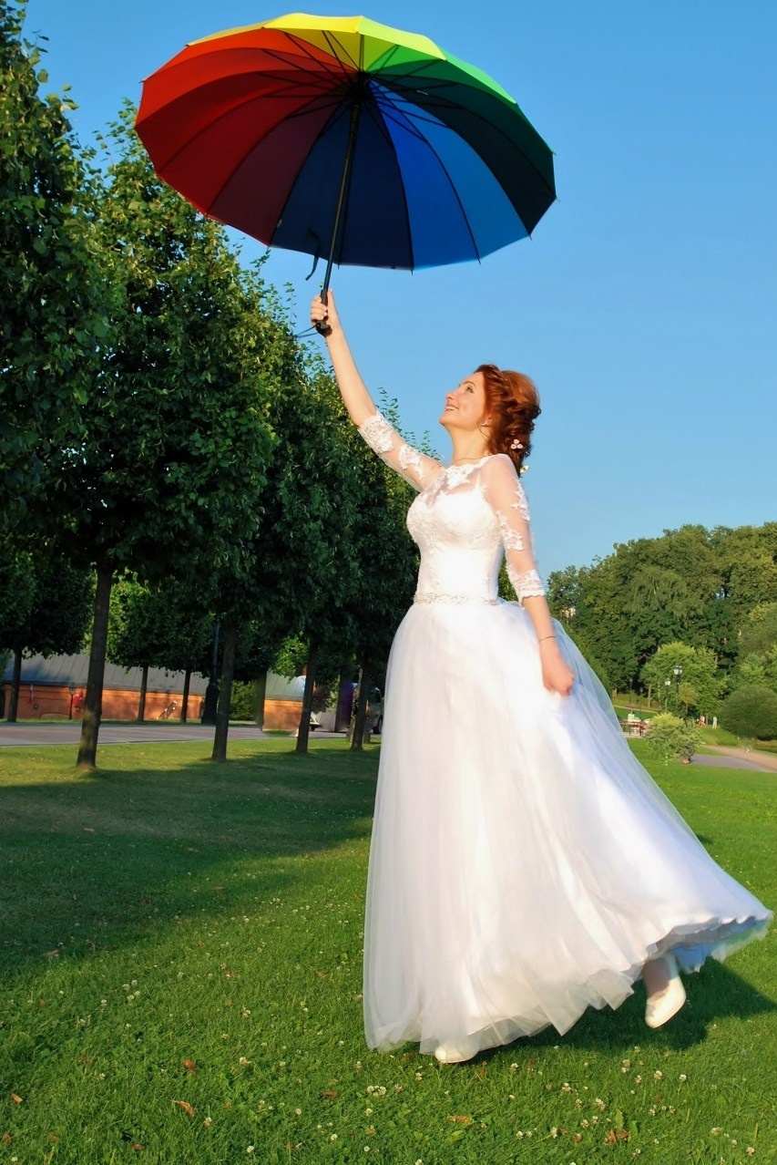 Свадебная фотосъёмка в Царицыно летом на закате, невеста держит в руках яркий разноцветный зонтик, яркое фото невесты в полный рост