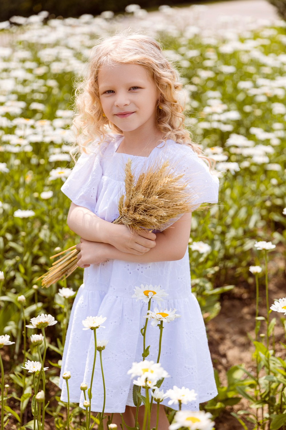 Девочка держит букет цветов, вокруг цветущие ромашки. 