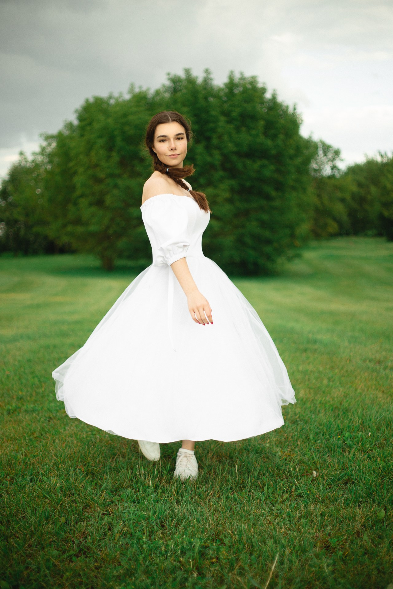 Девушка в белом платье гуляет летом по парку.