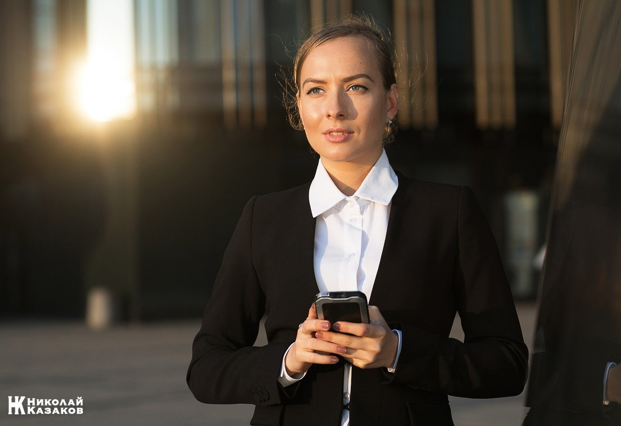 Портрет задумчивой бизнесвумен со смартфоном в руках в лучах заката.