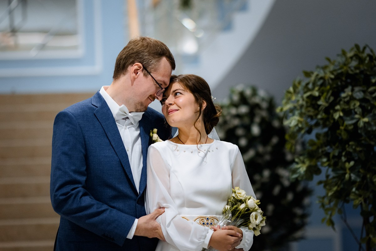 Жених и невеста стоят перед лестницей в холе ЗАГСа Красносельского района Санкт-Петербурга. Поясной план.