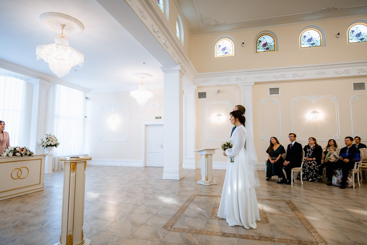 Жених и невеста в зале регистраций ЗАГСа Красносельского района Санкт-Петербурга идут ставить подписи