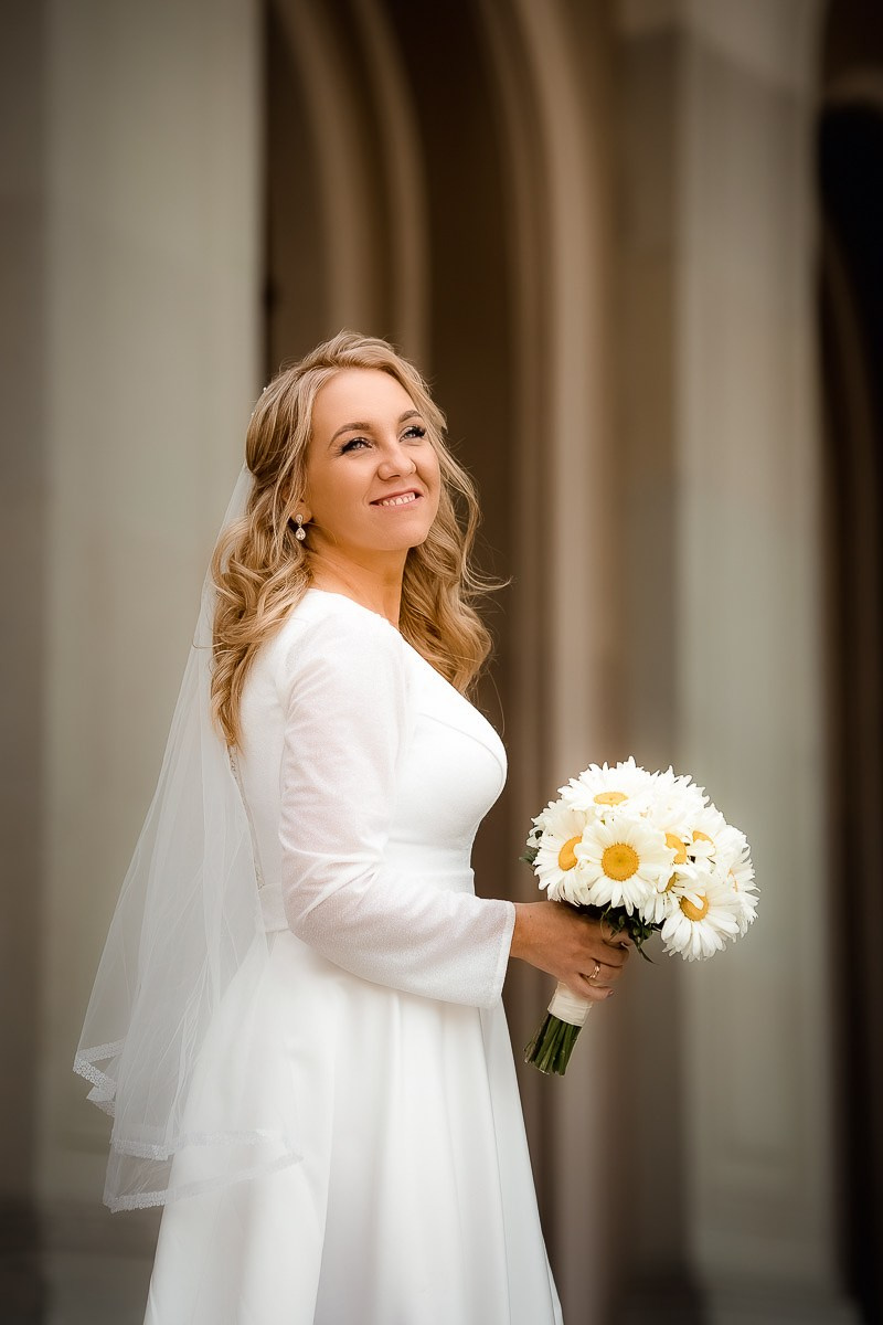 невеста смотрит в даль, стоя в арке на крыльце заксобрания в Санкт-Петербурге. Вертикальный поясной кадр.