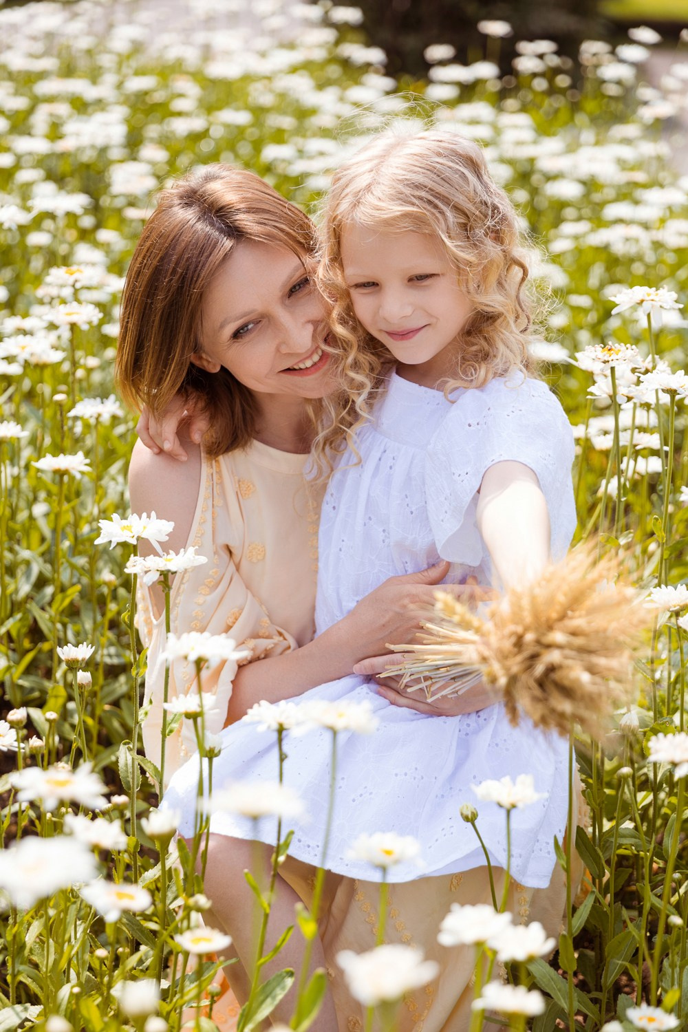 Мама сидит с дочкой на полянке с ромашками.