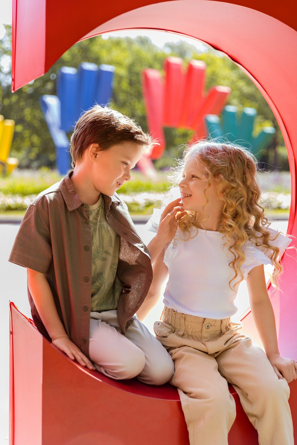 Мальчик с девочкой сидят на красной уличной инсталляции.