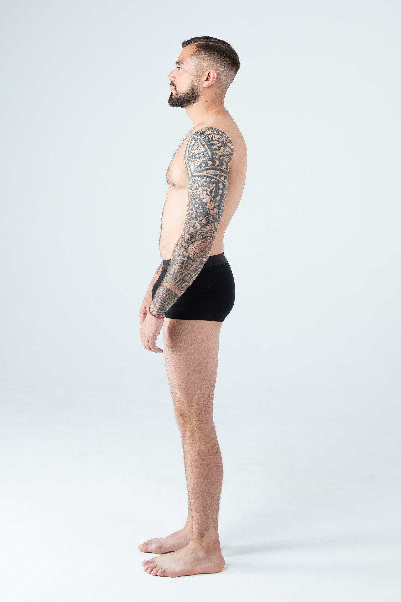 Мужчина модель с бородой с татуировками в черных трусах