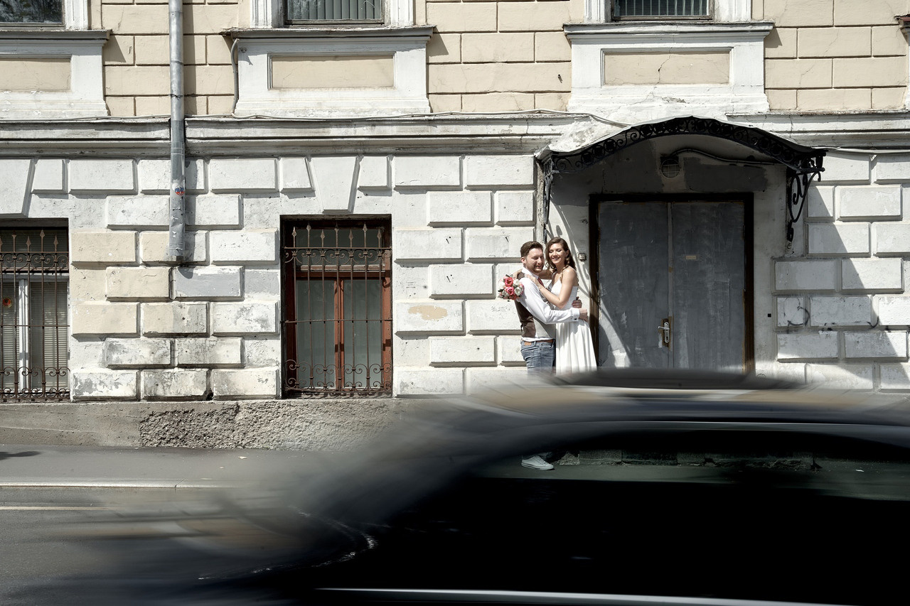 молодожены обнимаются у подъезда  на фоне проезжающей автомашины  Свадебная фотосъемка в Москве. Свадебный фотограф в Москве  Сергей Гаварос.