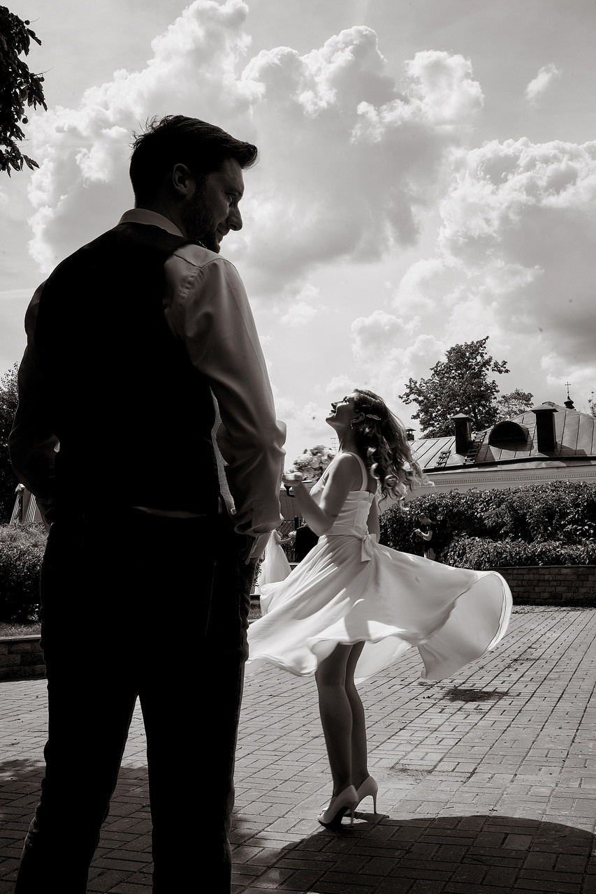 невеста с букетом кружится в коротком платье - на переднем плане силует жениха невеста заигрывает с женихом на улице Свадебная фотосъемка в Москве. Свадебный фотограф в Москве  Сергей Гаварос.