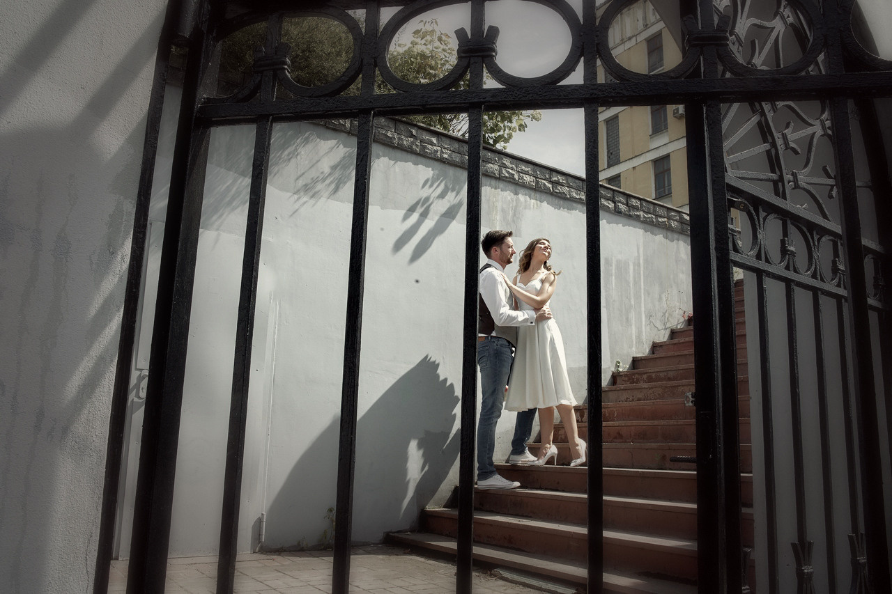 молодожены обнимаются на лестнице - вид через решетку забора Свадебная фотосъемка в Москве. Свадебный фотограф в Москве  Сергей Гаварос.
