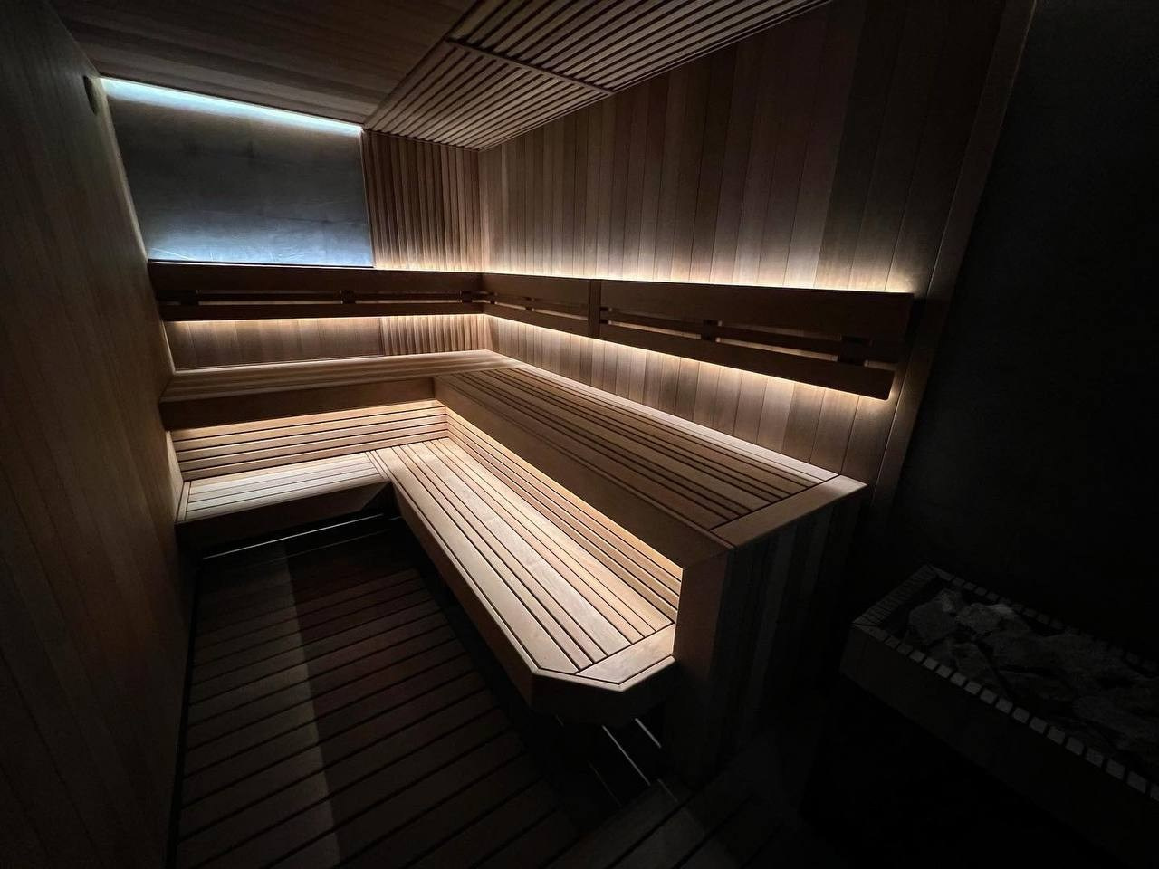 Сауна в Керро из разноширокой термоольхи. Ламповый свет термостойких лент и закарнизная подсветка плитки из талькохлорита 300×300мм. SaunaTopMasters