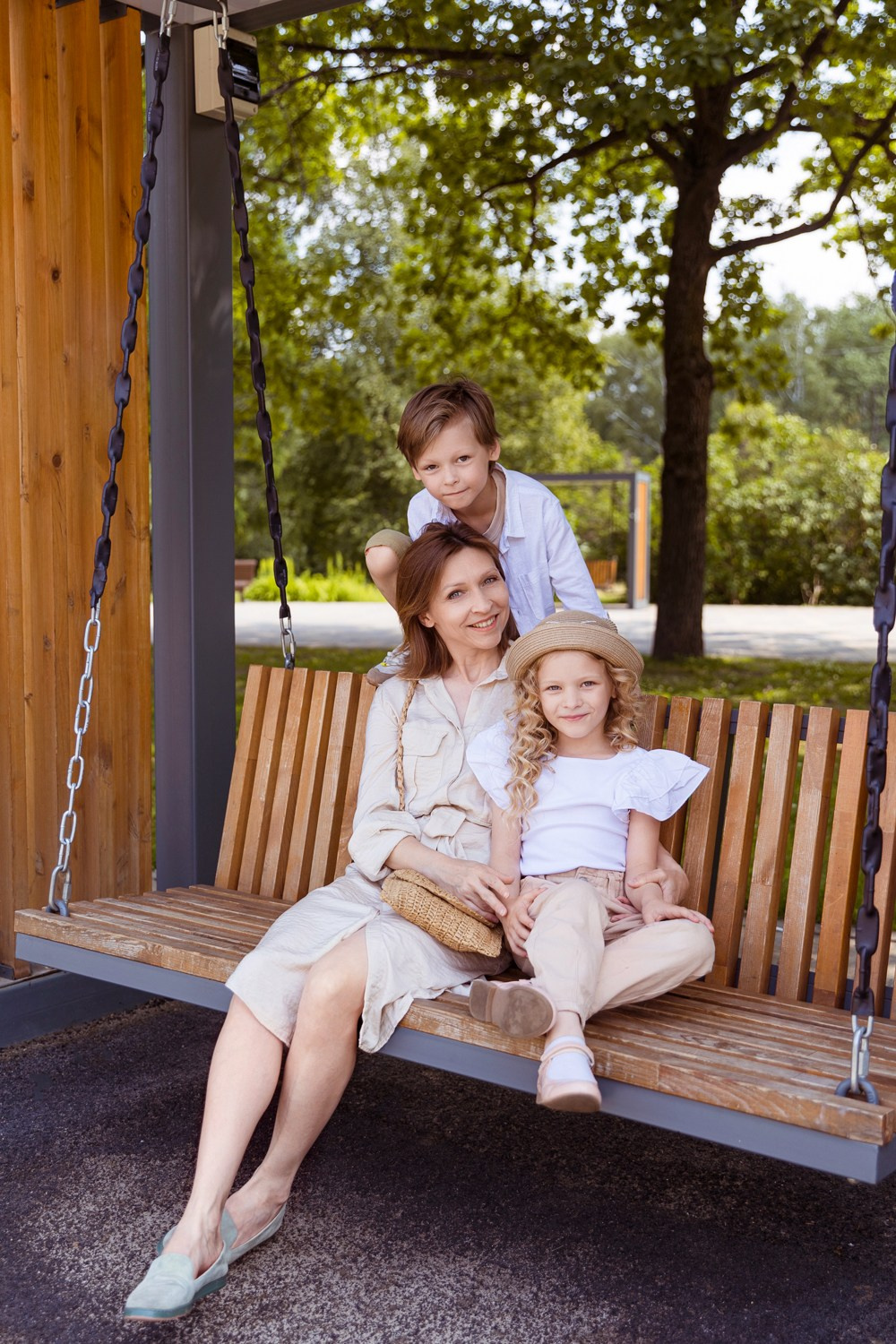 Мама с детьми сидит на лавочке в летнем, солнечном парке