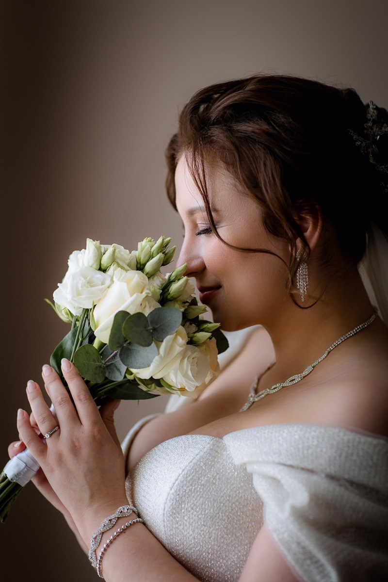 Невеста у окна нюхает букет. Крупный план вертикальный