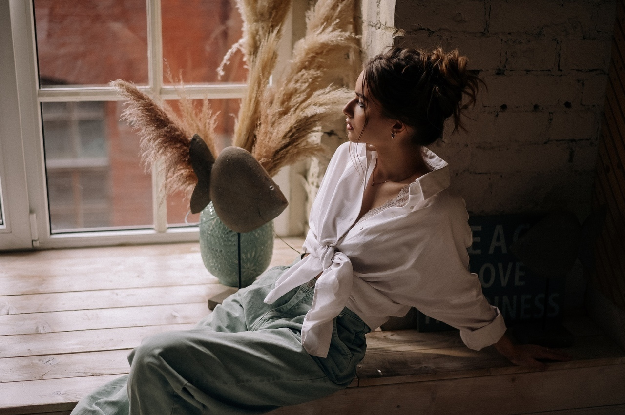 Девушка у окна в белой рубашке с высоким пучком , будто она не видит что ее снимают 