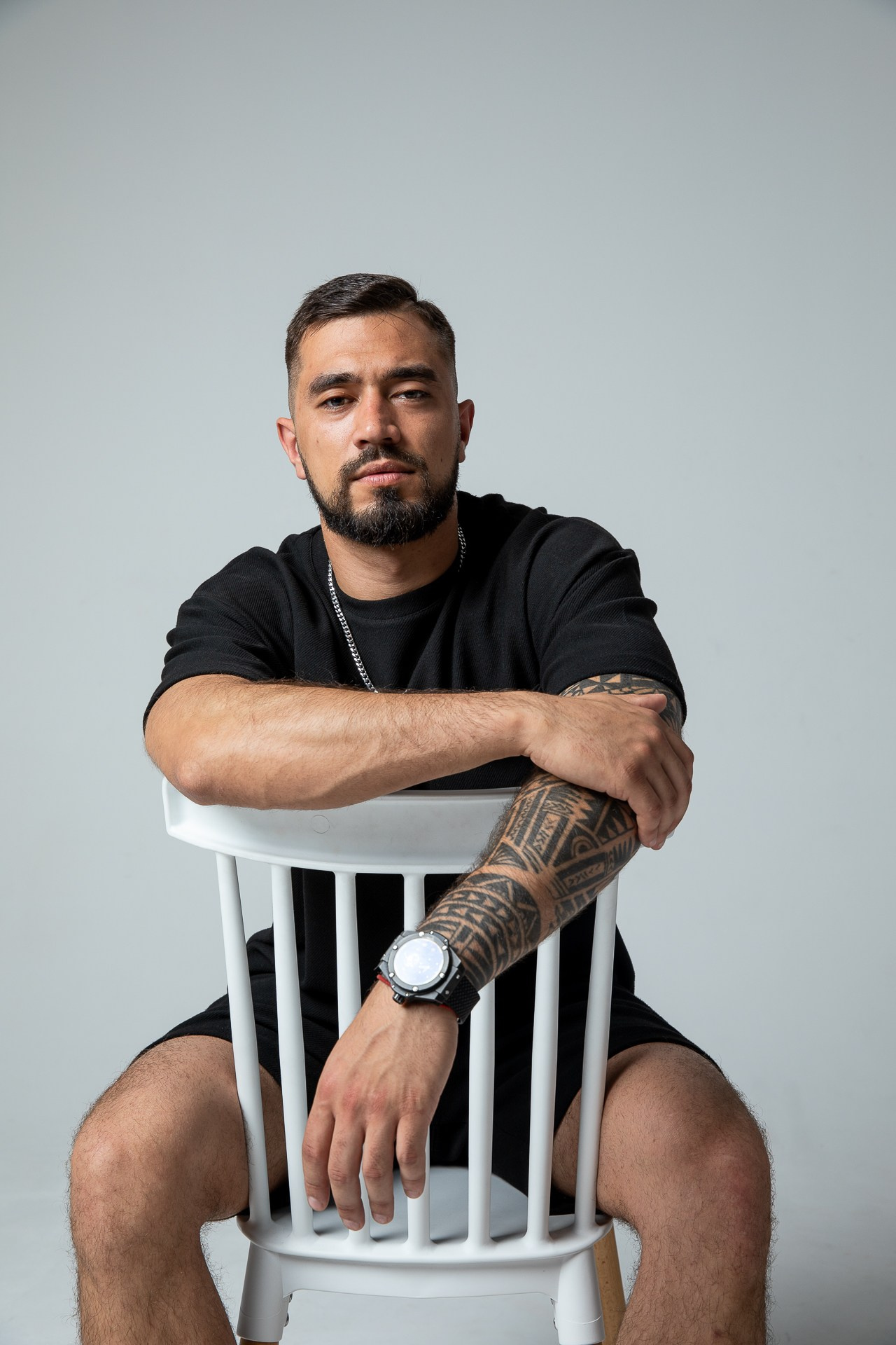 Смуглый мужчина в черной футболке и шортах сидит на стуле