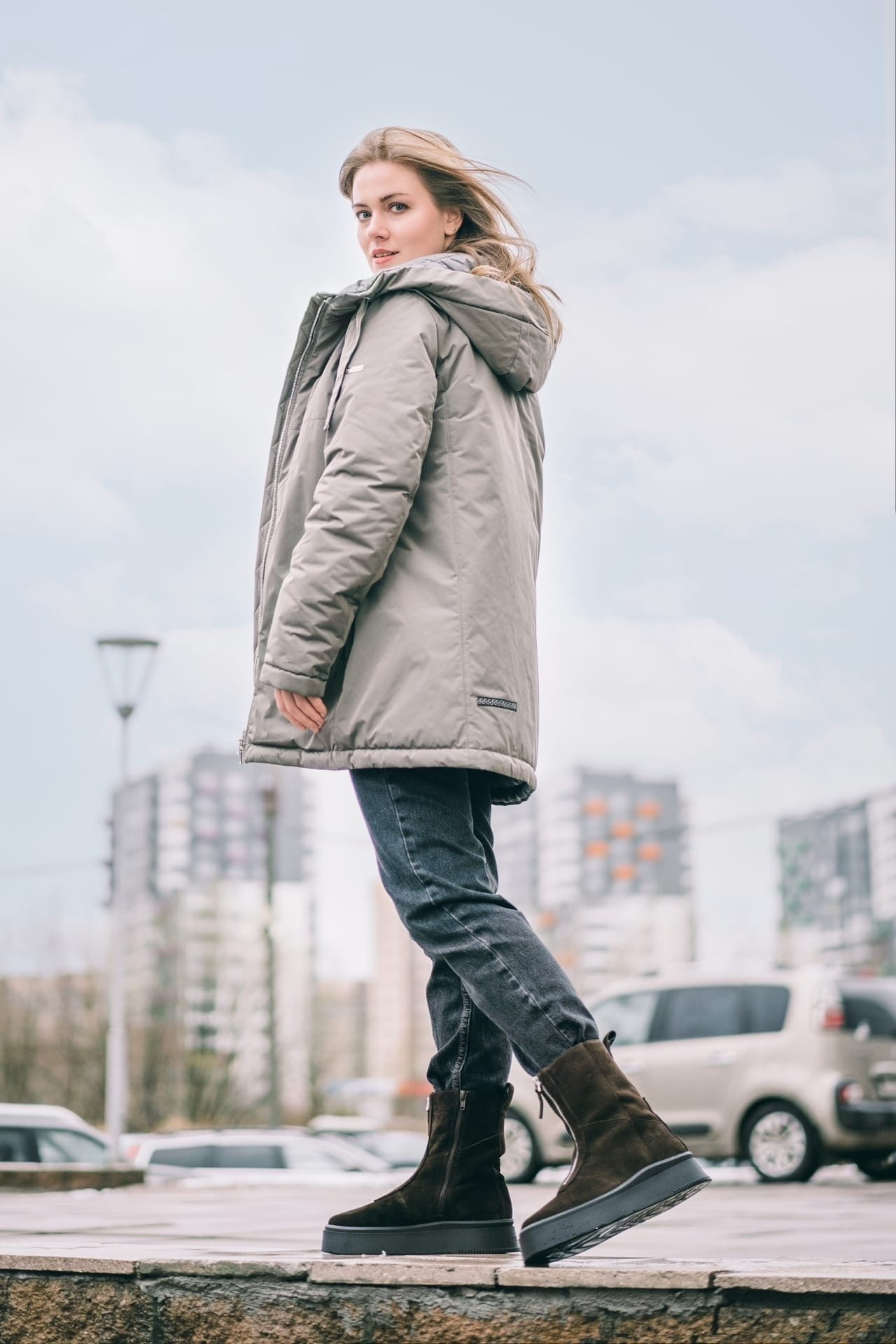 Девушка в куртке и джинсах на фоне города
