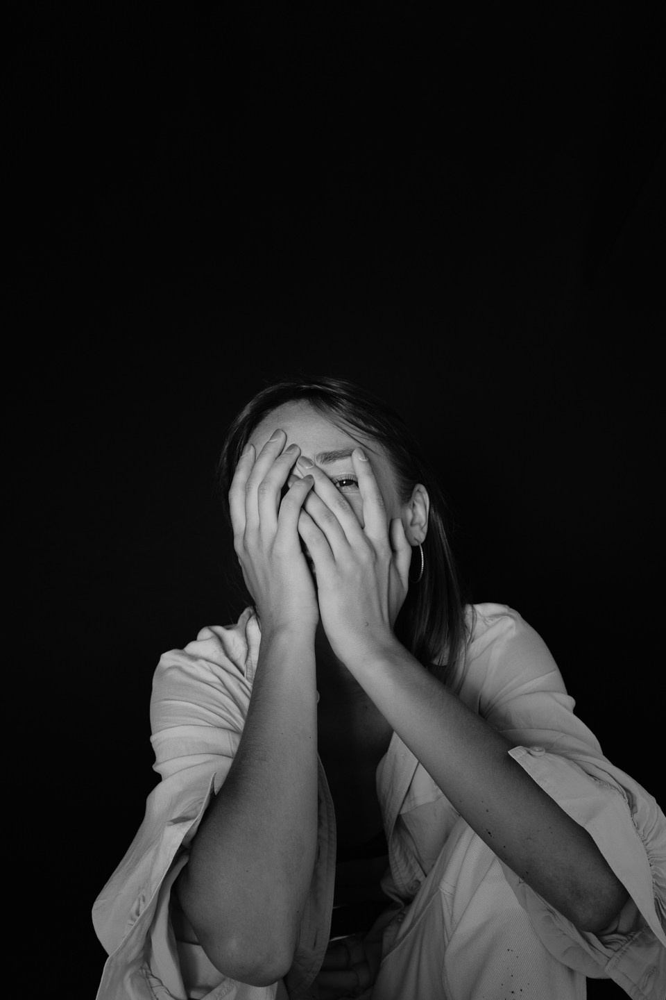 Фотоснимок девушки закрывавший лицо руками на черной фоне