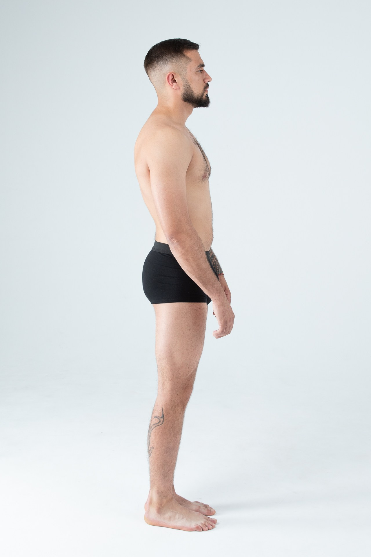 Мужчина модель с бородой с татуировками в черных трусах