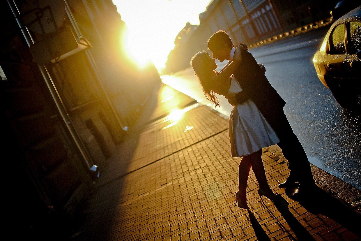 жених в черном обнимает невесту в коротком платье на фоне желтого закатного солнца