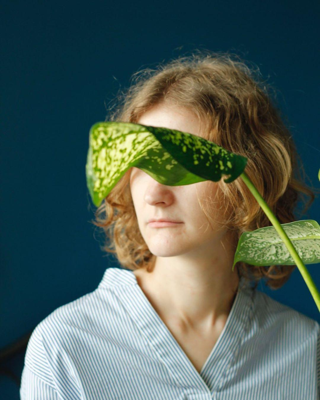Photo of woman with the home plant dieffenbachia closing her eyes whit a blue background