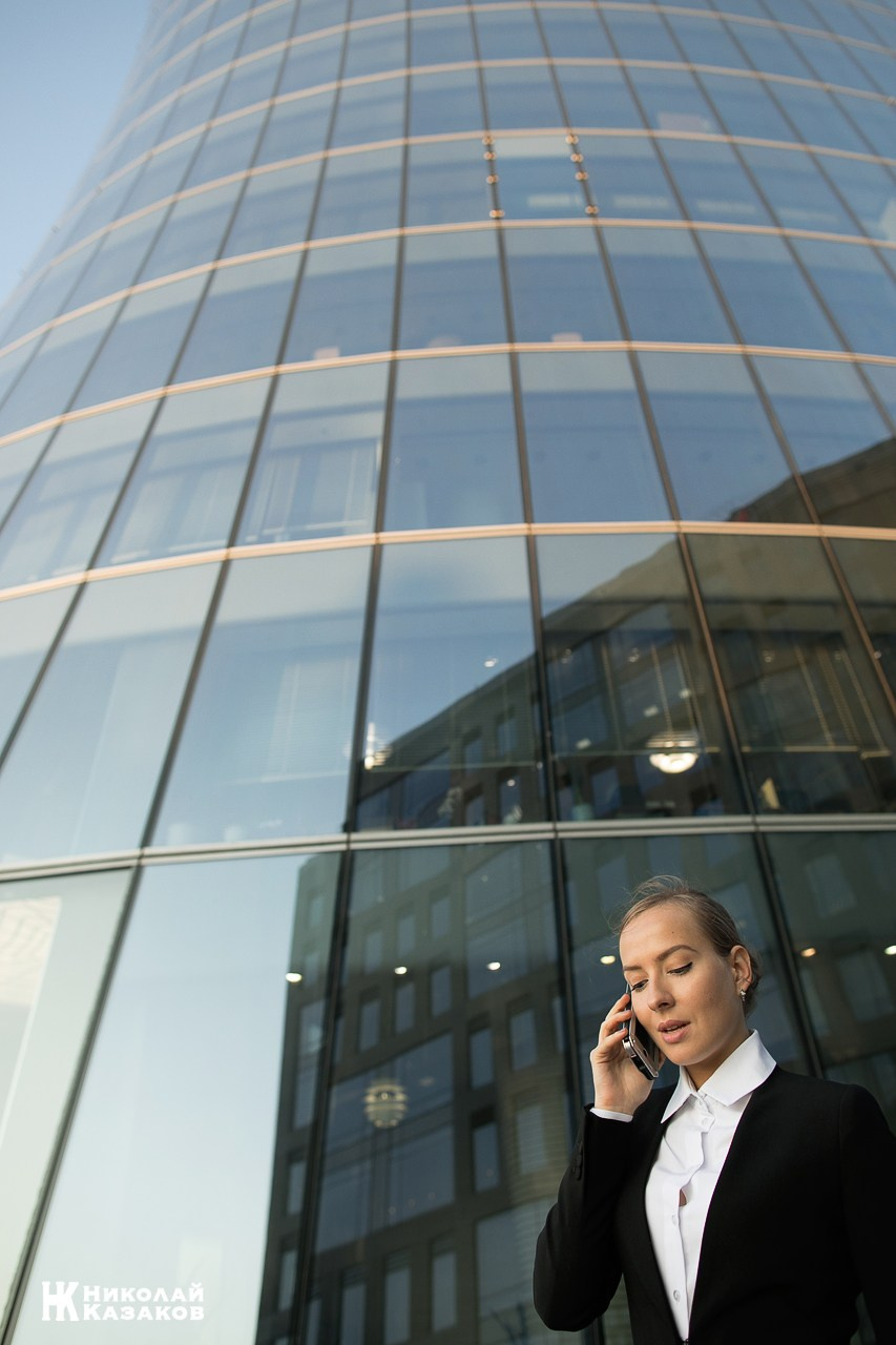 Деловая девушка общается с клиентом по смартфону на фоне стеклянного здания