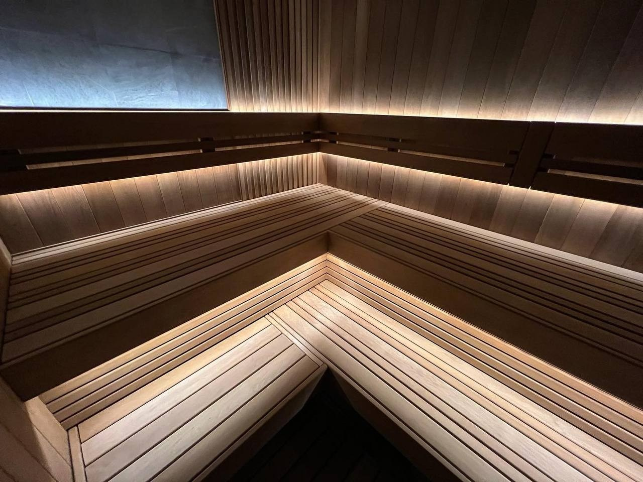 Сауна в Керро из разноширокой термоольхи. Ламповый свет термостойких лент и закарнизная подсветка плитки из талькохлорита 300×300мм. SaunaTopMasters