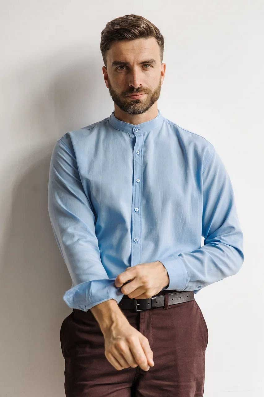 Мужчина с бородой в голубой рубашке и коричневых штанах