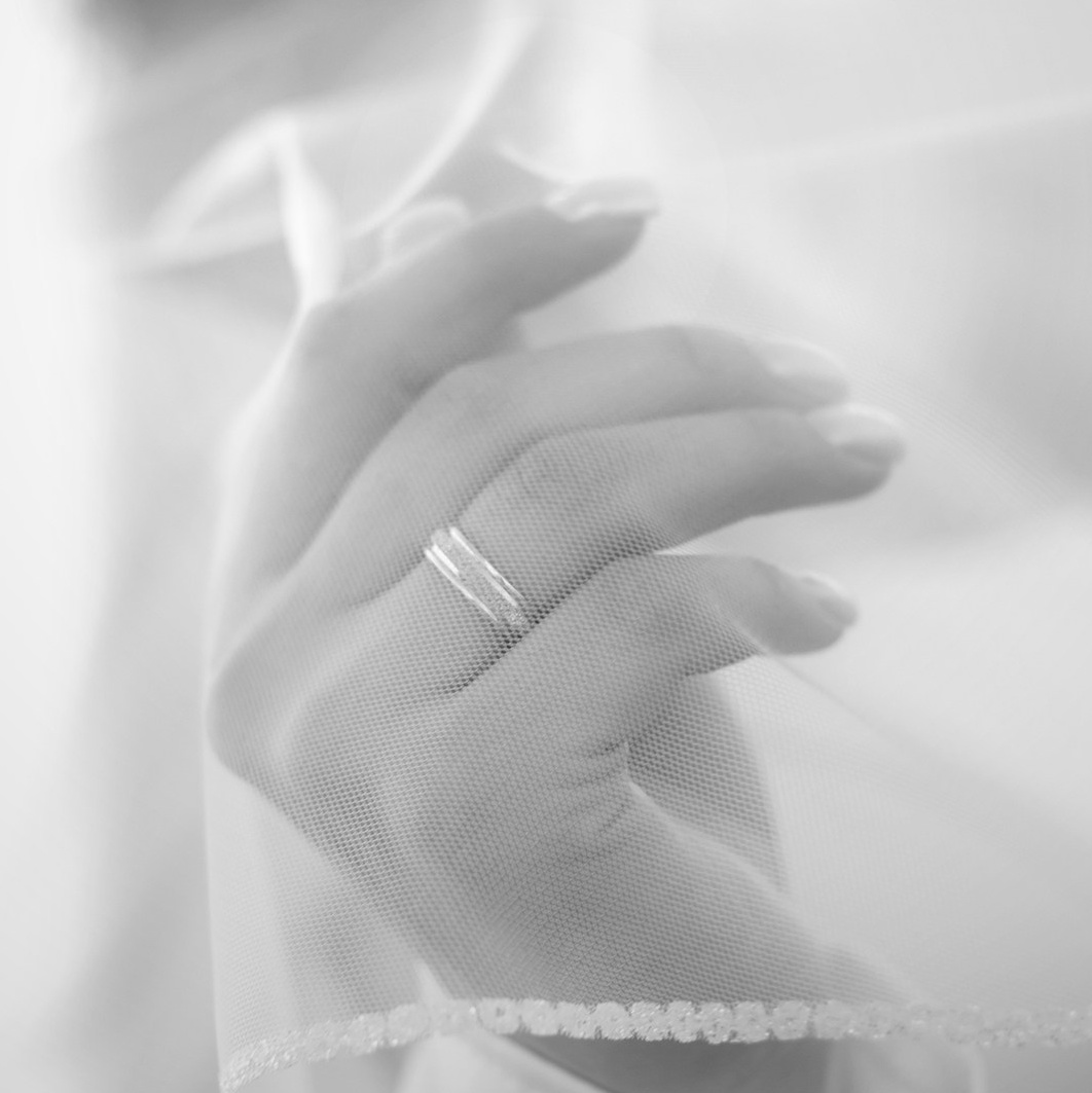 черно белое фото где изображена рука невесты с кольцом на переднем плане, покрытая полупрозрачной фатой