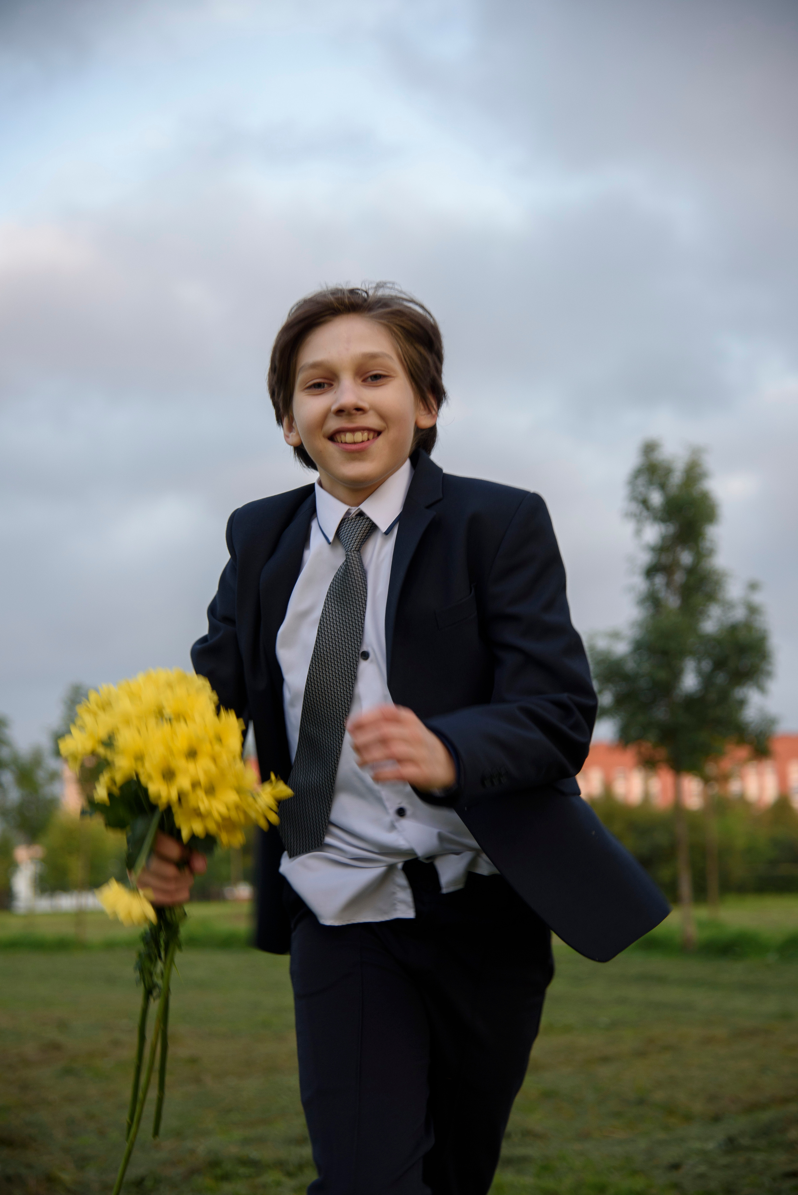 мальчик подросток в костюме и белой рубашке с букетом желтых цветов бежит навстречу