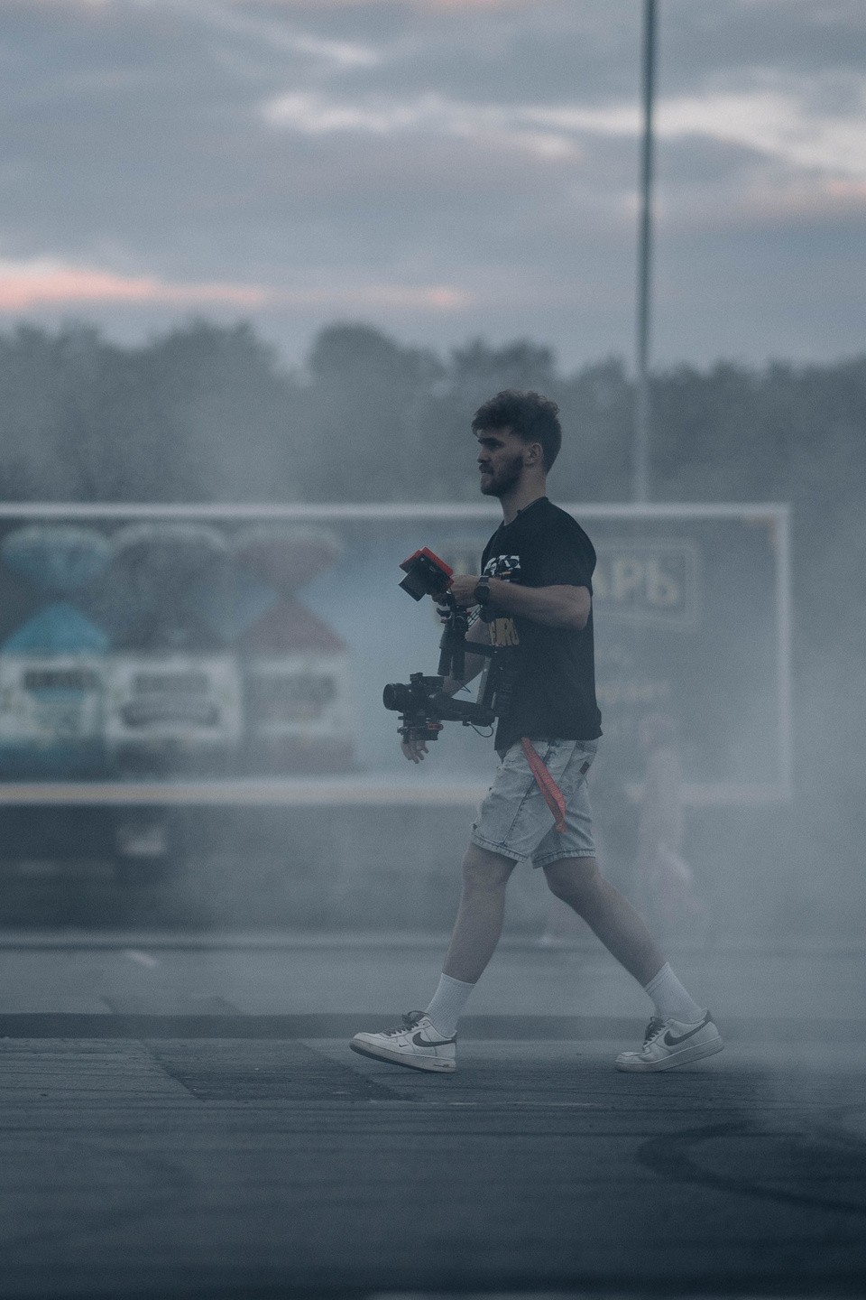 оператор идет по парковке в дыму от шин автомобилей